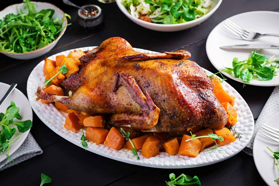 Homemade baked duck. Crispy whole roast duck. Thanksgiving or Christmas dinner. Roast duck with thyme and pumpkin on rustic wooden table.