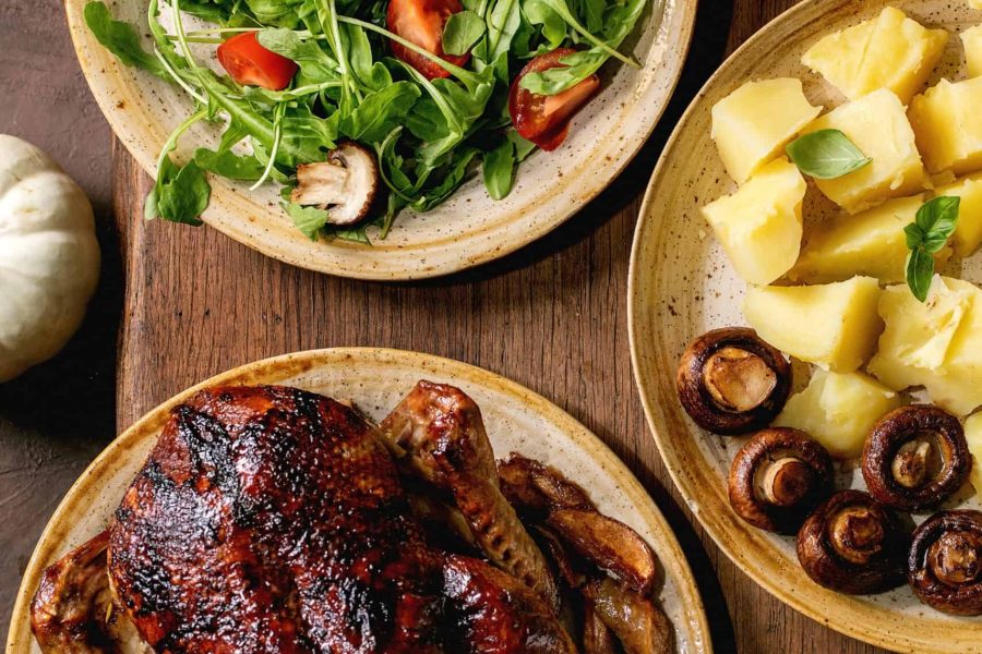 Holiday table with classic dishes roasted glazed duck with apples, boiled potatoes, green salad and sauce on dark wooden table with autumn decor. Flat lay
