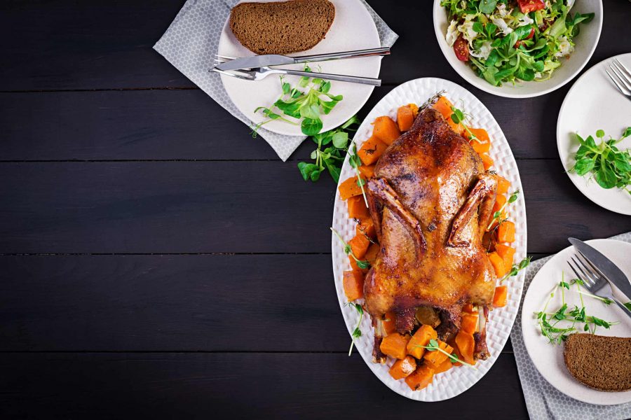 Homemade baked duck. Crispy whole roast duck. Thanksgiving or Christmas dinner. Roast duck with thyme and pumpkin on rustic wooden table. Top view, overhead